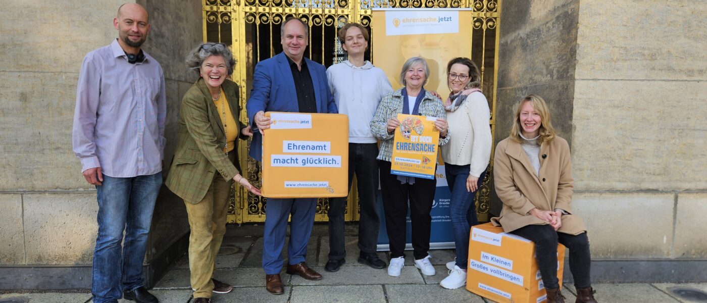 Menschen stehen vor der Goldenen Pforte des Dresdner Rathauses. Sie halten ein Schild: Ehrenamt macht glücklich.