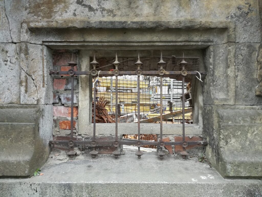 Das Bild zeigt einen Kohleeingang für den Keller der von einem alten Gitter verschlossen ist