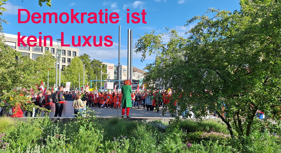 Menschen auf dem Postplatz. Eine Rednerin spricht. Darüber steht: Demokratie ist kein Luxus.