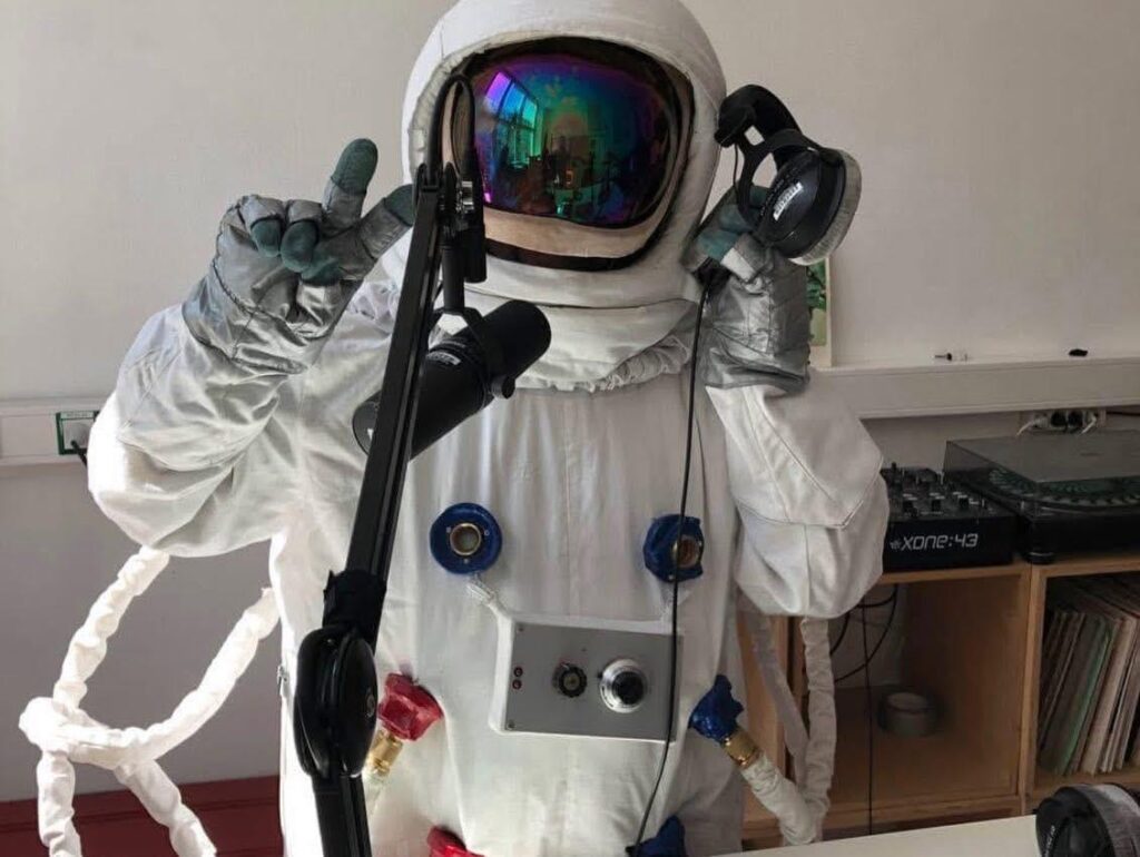 Das Bild zeigt eine Person in einem Austronaut*innenkostüm im Aufnahmestudio hinter einem Mikrophon.