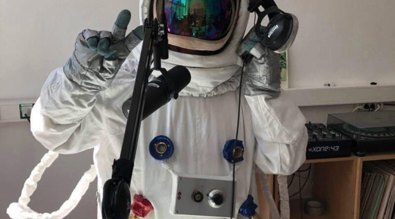 Das Bild zeigt eine Person in einem Austronaut*innenkostüm im Aufnahmestudio hinter einem Mikrophon.