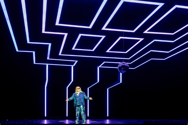 Das Bild zeigt eine Person in einem anzugähnlichen Kostüm. Über und hinter ihr sind LED-Lichtstreifen.