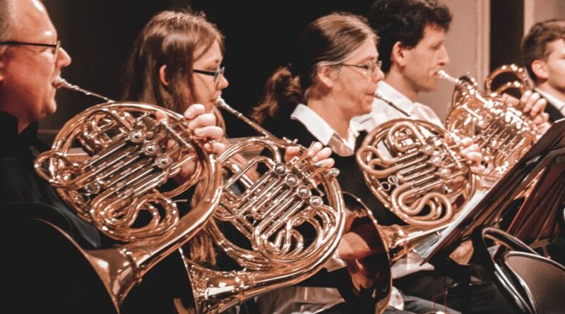 Das Bild zeigt von der Seite 5 Menschen welche alle ein Horn (Instrument) in der Hand haben und es spielen.