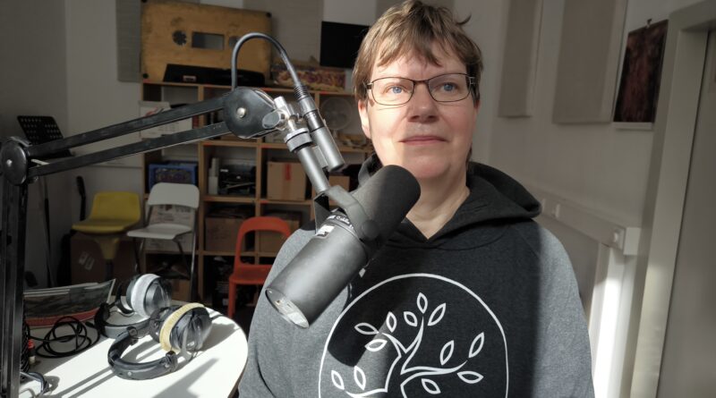 Das Bild zeigt eine ältere Frau in eine Aufnahmestudio. Die Frau hat ein Mikrophon schräg vor ihrem Gesicht.
