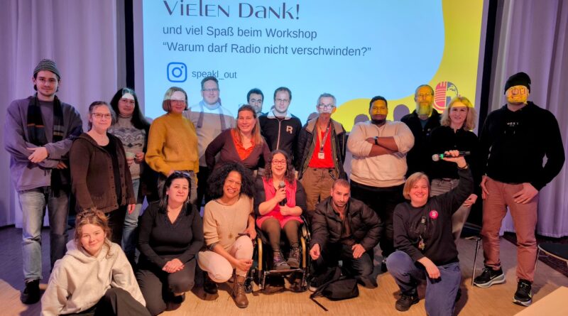 Das Bild zeigt eine Gruppe von 19 Menschen, die vor einer großen Leinwand stehen die angestrahlt wird. Auf der Leinwand wird angestrahlt: Vielen Dank! und viel Spaß beim Workshop "Warum darf Radio nicht verschwinden?