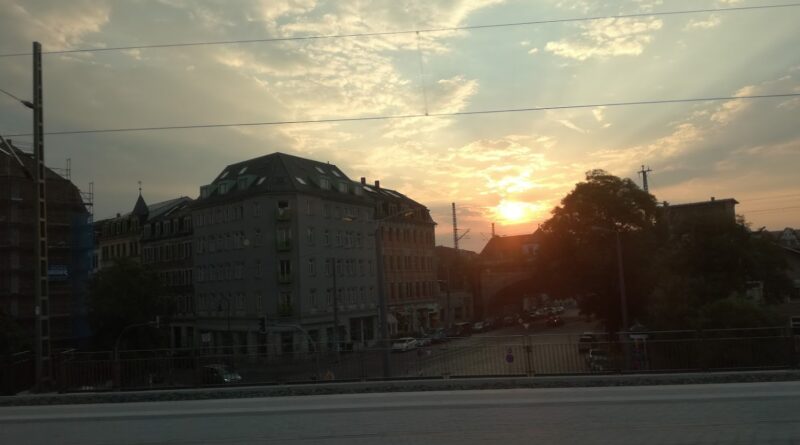 Zu sehen ist eine Häuserecke der Dresdner Neustadt, fotografiert vom S-Bahnhof Bischofsplatz. Am Himmel ist der Sonnenuntergang zu sehen.