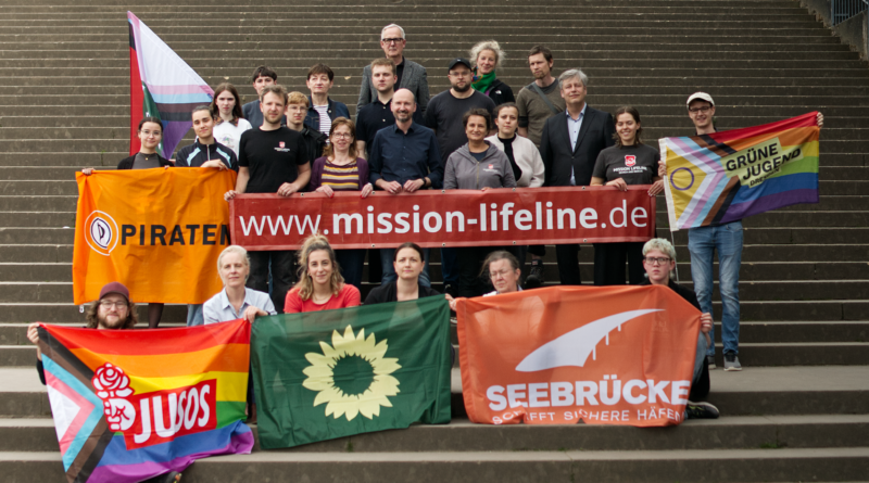 Menschen die Banner auf einer Treppe hochhalten. Auf den bannern sthet: Mission Lifeline, Piraten-Partei, Jusos (Junge Soziale), Seebrücke und Grüne Jugend.