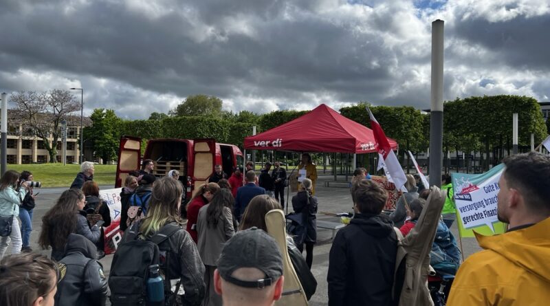 Auf dem Bild sind mehrere Menschen die vor einem roten Pavillon stehen. Auf dem Pavillon steht ver.di. Sie halten Banner hoch, auf einem steht: Versorgung braucht gerechte Finanzierung.